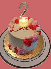 A round white, red, and pink rose icing cake with a number 2 candle on it and the word Love written on the cake on a gold platter