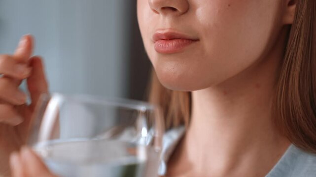 A woman takes a vitamin supplement and drinks water at home