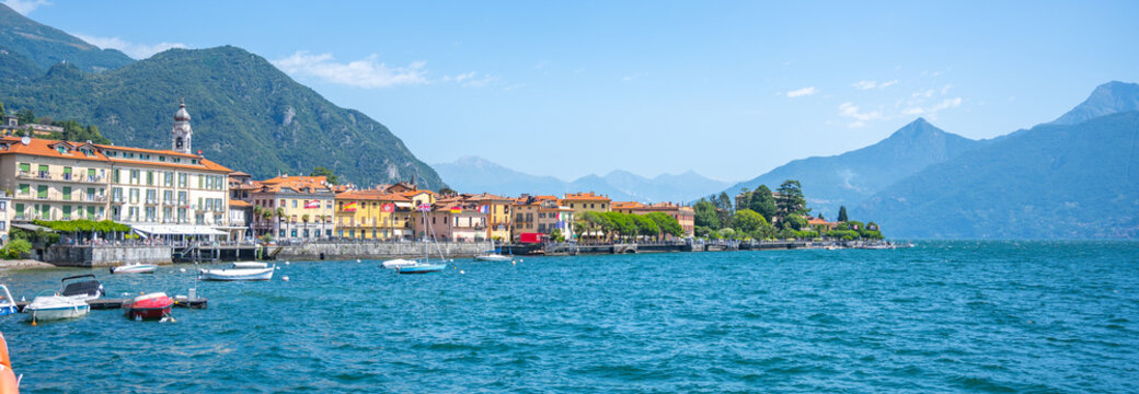 Menaggio showcases its picturesque waterfront, adorned with charming buildings and boats bobbing on the clear blue waters of Lake Como under a vibrant sky.