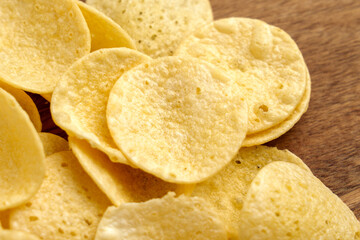 Many golden potato chips on brown wooden table. Top view. 