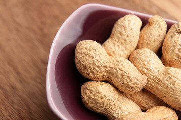 Roasted peanuts with shells in a red ceramic bowl. Unshelled organic nuts. Macro shot. 