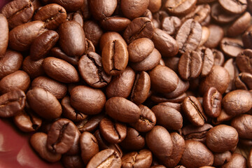 Aromatic whole roasted coffee beans in red ceramic bowl. Macro shot