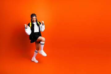 Joyful teenage student in casual outfit posing in a vivid studio with bright orange background...