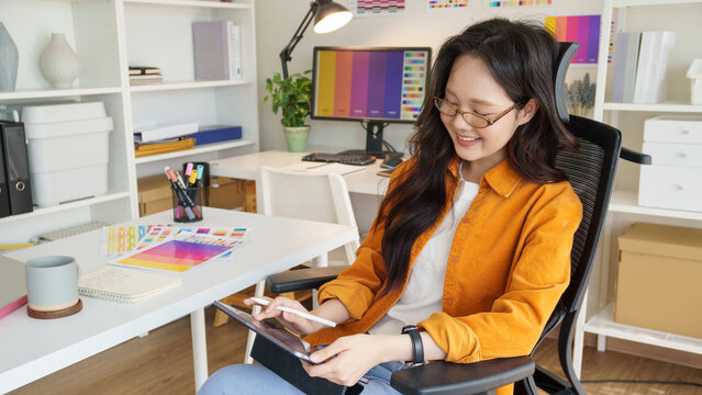 Young graphic designer smiling while working on a digital tablet in a modern creative studio.