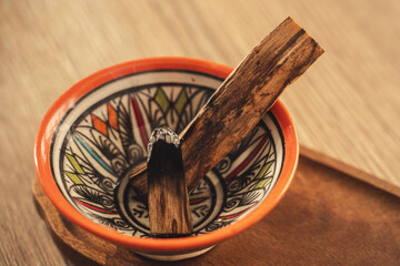 Smoldering Palo Santo Sticks in Colorful Ceramic Bowl on Wooden Tray