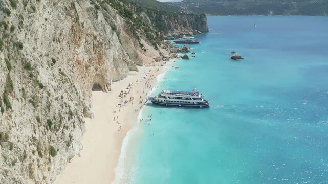 A scenic view of a sandy beach on Ithaki island, Greece. People are swimming and relaxing under the sun while a large cruise ship anchors nearby in the turquoise sea. Perfect summer travel atmosphere.