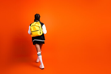 Teenage girl with a yellow backpack stands on an orange background, wearing a casual and stylish...