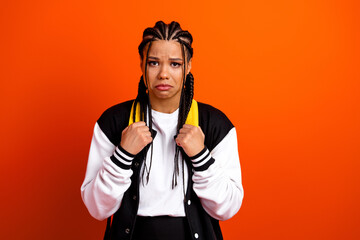 Teenage girl with braided hairstyle expressing concern against vibrant orange background in casual...