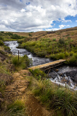 A small bridge crossing a fast-flowing mountain stream in the grasslands of the Drakensberg mountains of South Africa.