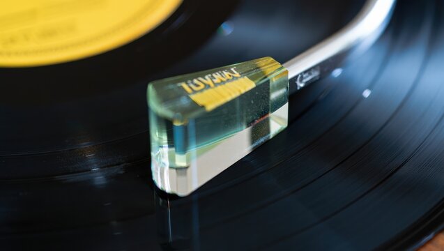 Close-up of vinyl turntable tonearm with transparent glass cartridge.