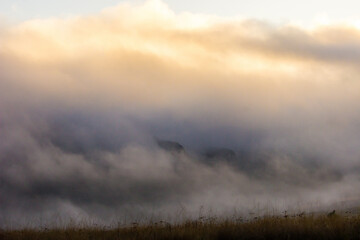 Thick mist cover tinted golden by the light of rising sun, with just small parts of the mountains below peeking out in the Drakensberg mountains of South Africa.