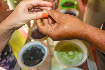 Hand of a Sri Lankan man holding a precious stone, many types and colors in bowls with water on a table surrounded by tourists, Moonstone Mine tour, Sri Lanka.