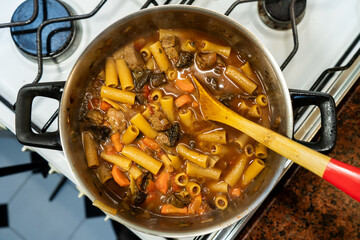 Chef preparing beef and vegetable stew with pasta in a pot on the stove