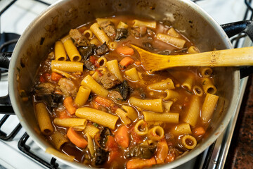 Chef cooking beef stew with rigatoni pasta and mushrooms in pot