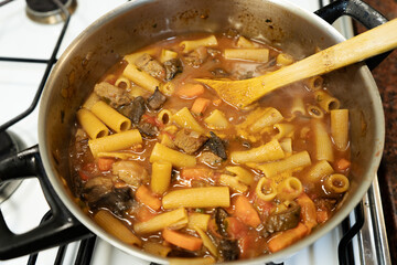 Chef cooking pasta with meat and vegetables in a pot on the stove