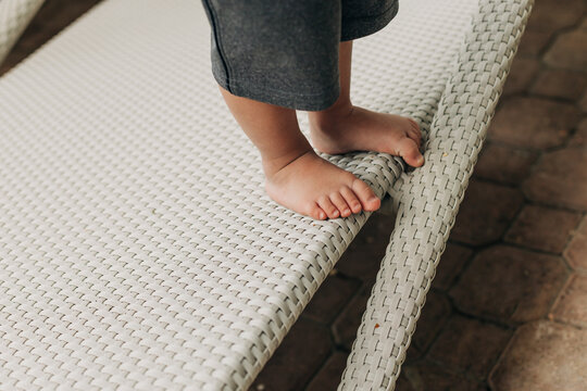Toddler explores balance on the edge of a sun lounger near a pool in the afternoon sunlight