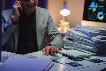 Businessman calculating and speaking on phone with graphs on computer screen at night