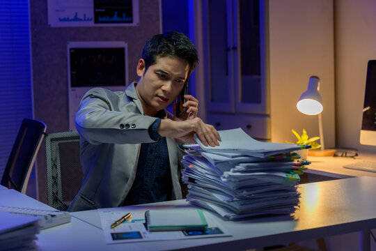 Asian businessman working late and checking documents while having phone call