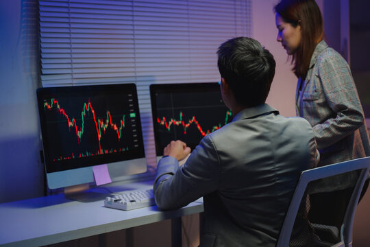 Stockbrokers analyzing cryptocurrency investment risk using dual monitors in office