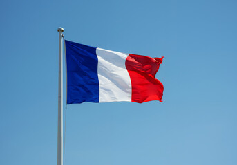 Naklejka premium A French flag waving against a clear blue sky mounted on a metal pole
