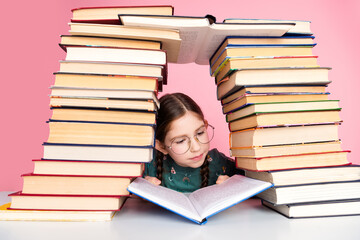 Young girl reading a book surrounded by colorful stacked book against a pink background, showcasing...