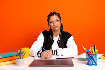 Teenage girl with braids studies at a colorful desk with an orange background, symbolizing...