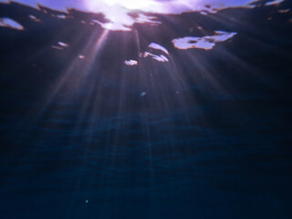 Dark blue ocean surface seen from underwater. Abstract waves underwater and rays of sunlight...
