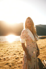 A woman in a floral dress stands on a beach at sunset