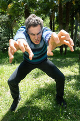 Man crouching and doing scary gesture in a park