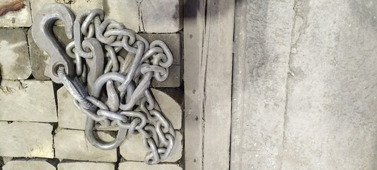 Heavy duty metal chain and hook on a brick and concrete surface. Industrial lifting equipment with a rustic, worn texture. Metal chain link hook background. Grunge style industrial background.