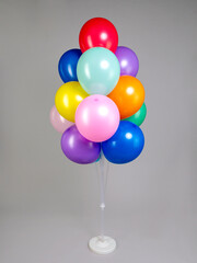 Multicolored balloons on white plastic stand isolated on gray background