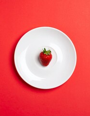 Single Strawberry on White Plate Against Red Background