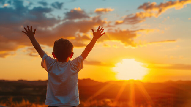 A young boy is standing in a field with his hands raised in the air