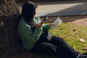 Young woman entertained watching her cell phone while reading in the park
