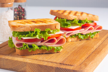 Close-up of two sandwiches with bacon, salami, prosciutto and fresh vegetables on rustic wooden...