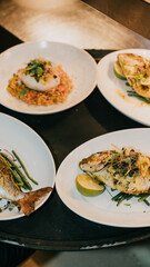 A table with four plates of food, including fish, vegetables, and a dessert. The plates are arranged in a way that makes the food look appetizing and inviting. Scene is one of indulgence and enjoyment