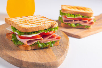 Close-up of two sandwiches with bacon, salami, prosciutto and fresh vegetables on rustic wooden...