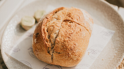 A piece of bread with a butter knife on a white plate. The bread is cut in half and has a butter knife on top of it
