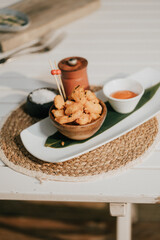A plate of fried food with a bowl of sauce and a small container of sauce. The plate is on a table with a woven mat underneath it