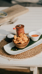 A plate of fried food with a bowl of sauce and a pepper grinder. The plate is on a table with a woven mat underneath it