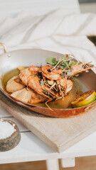 A plate of shrimp and vegetables is served on a wooden table. The shrimp are cooked and seasoned, and the vegetables are fresh and green. The dish looks delicious and inviting