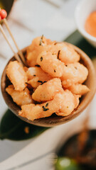A bowl of fried food with a green leaf on top. The bowl is wooden and the food is golden brown