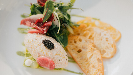 A plate of food with a salad and bread on the side. The salad is garnished with a sauce and has a few pieces of meat on top. The bread is to the right of the salad and is toasted