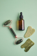 Facial massage set made of natural materials and components, natural cosmetics in amber glass and facial massagers made of natural stone, top view, green background