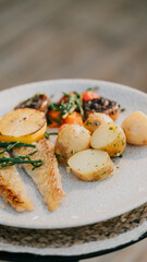 A plate of food with a fish and potatoes on it. The plate is white and the food is colorful