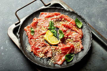 Slices of fresh beef carpaccio with basil and parmesan cheese in a black plate on the black background close up