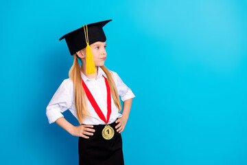 Little girl in graduation cap with a gold medal posing confidently against a blue backdrop,...