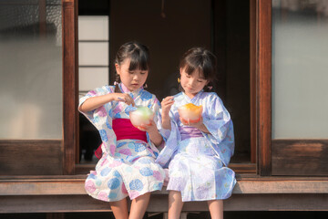 縁側でかき氷を食べる浴衣姿の姉妹