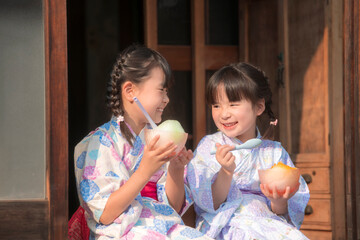 縁側でかき氷を食べる浴衣姿の姉妹