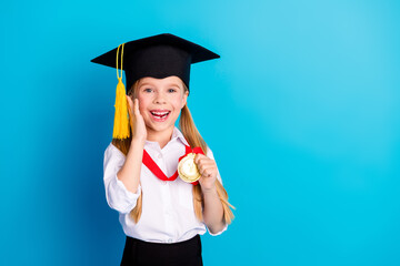 Portrait of a cheerful young schoolgirl wearing a graduation cap and medal, expressing excitement